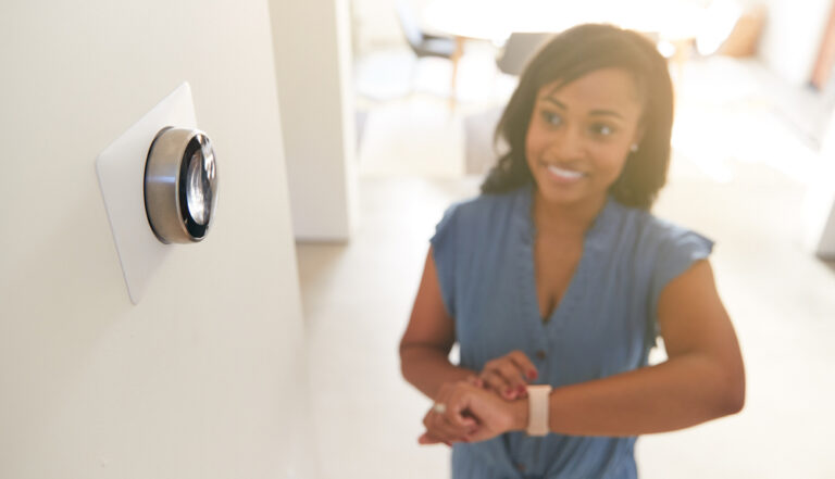 Homeowner using her smartwatch to adjust the smart thermostat temperature.